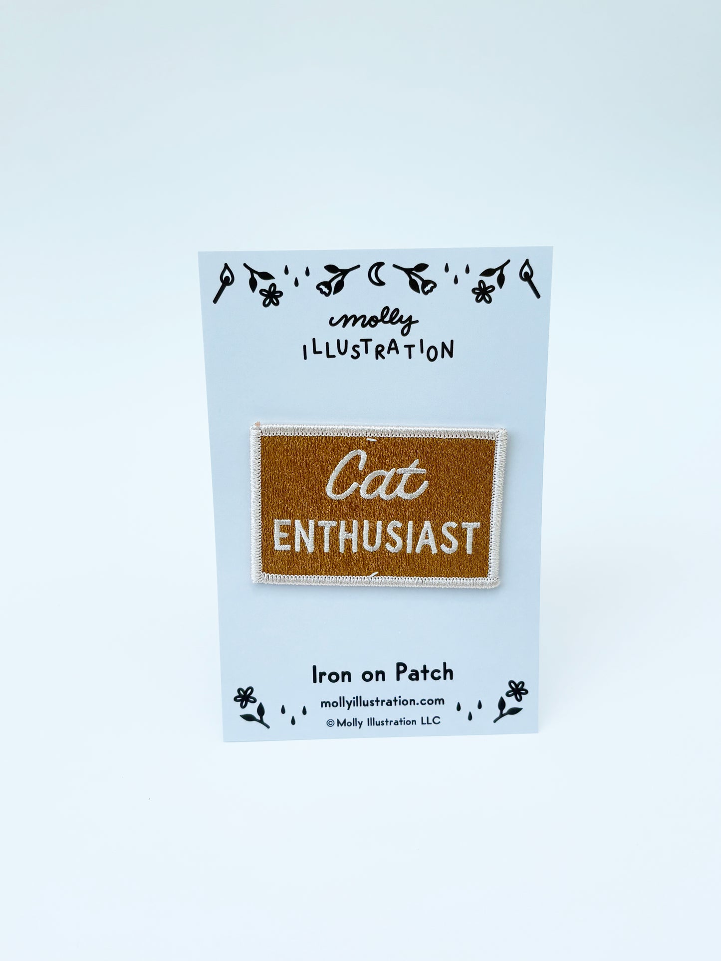 Iron on patch labeled 'Cat Enthusiast' on a blue backing card with 'molly illustration' branding.