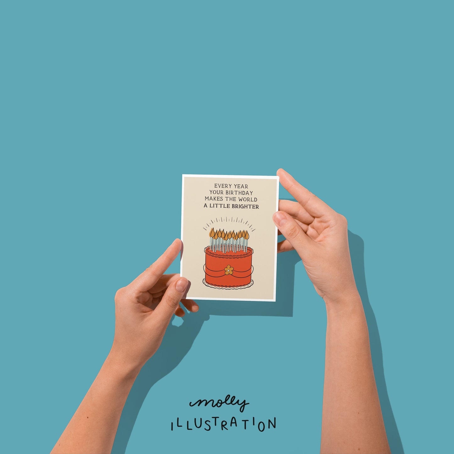 hands holding an illustrated greeting card that reads "every year your birthday makes the world a little brighter" above a red birthday cake covered in lit candles