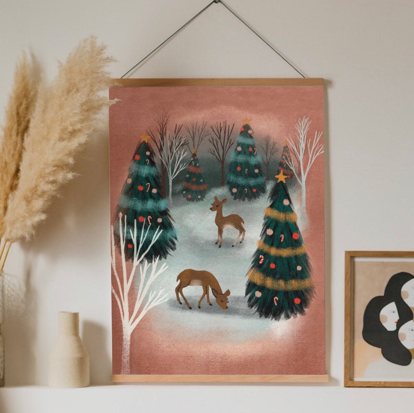 A mid century inspired art print of a snowy christmas forest scene. There are two deer standing among many pine trees that are decorated with garlands and ornaments.