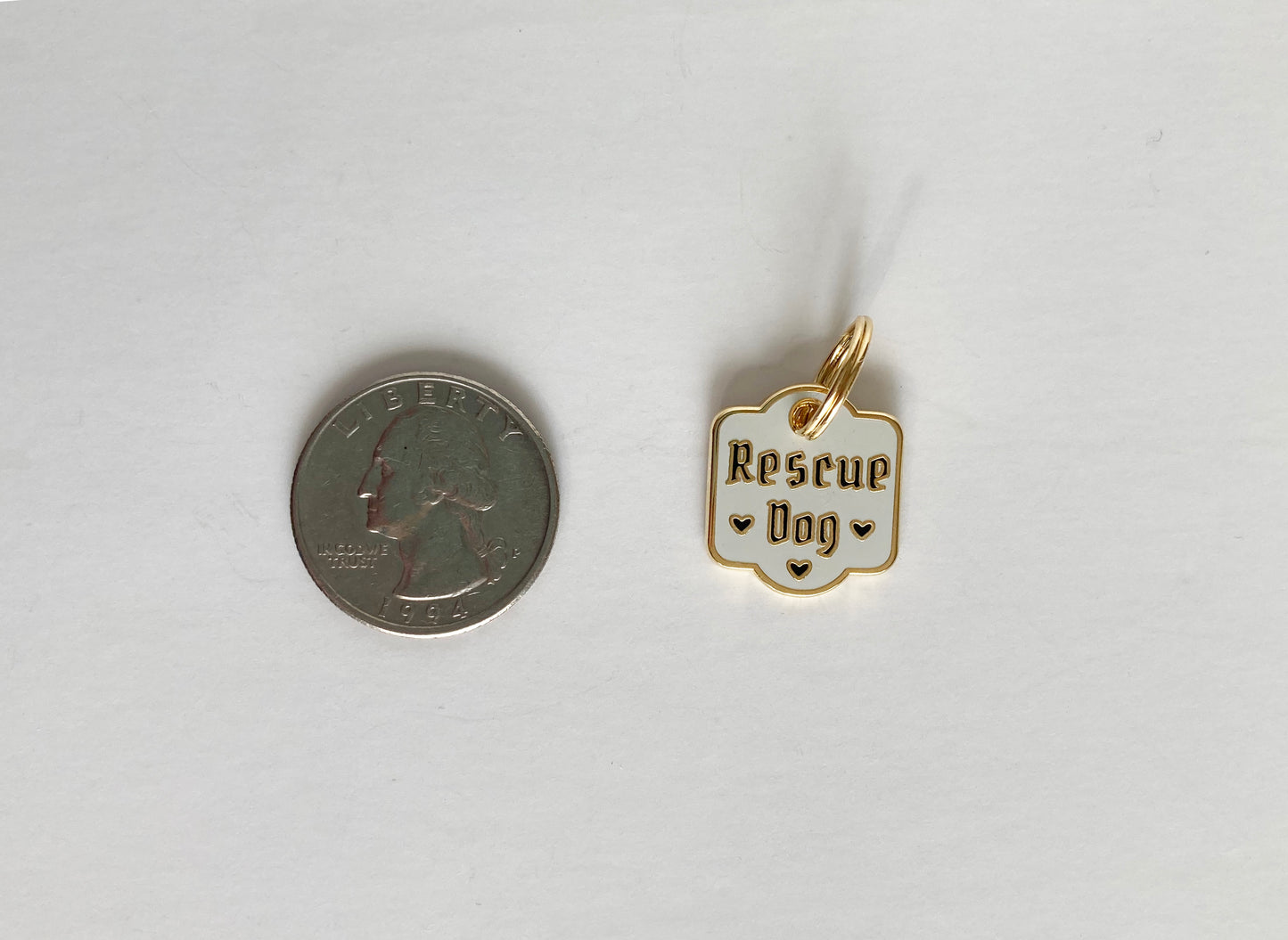 A hard enamel pet collar charm that reads “Rescue Dog” next to a quarter.