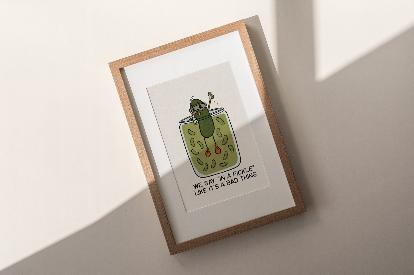 a white and green illustrated art print of a pickle swimming in a pickle jar that reads "We say in a pickle like it's a bad thing.”