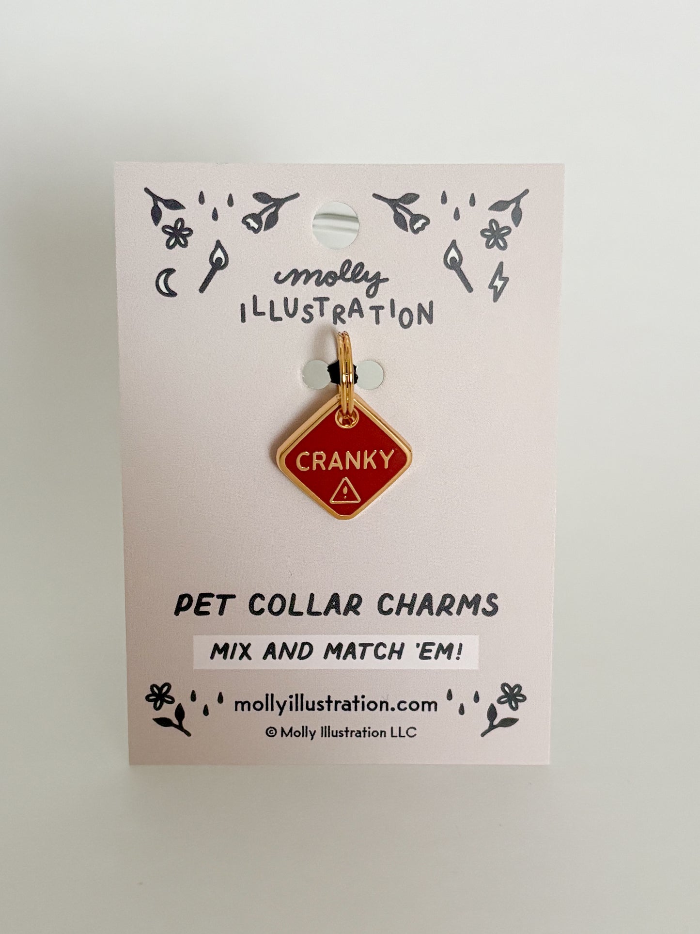 Pet collar charm that reads "Cranky" on a Molly Illustration branded card with a white background