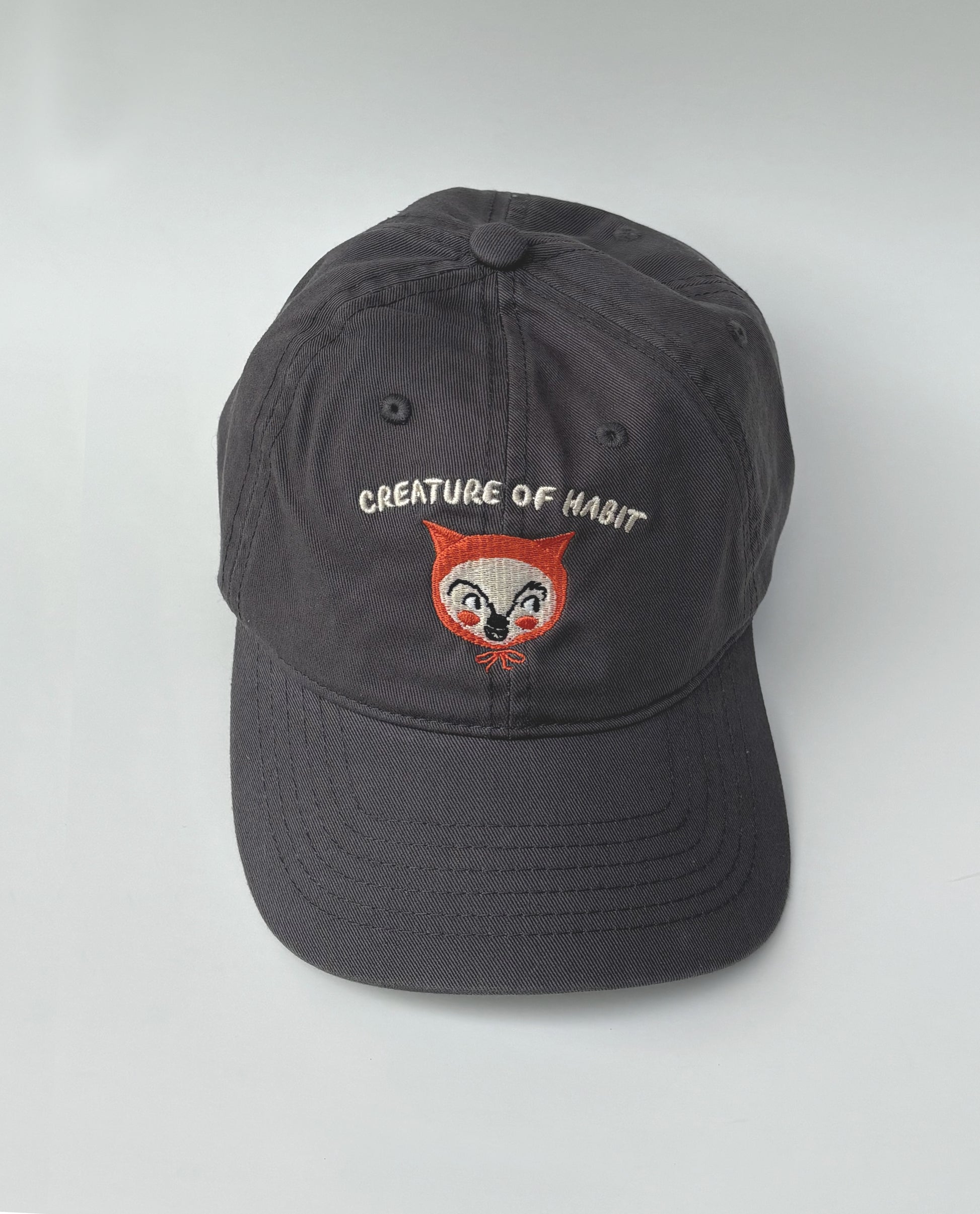 Dark gray cap with embroidered creature face and text on a white background