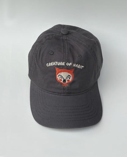 Dark gray cap with embroidered creature face and text on a white background