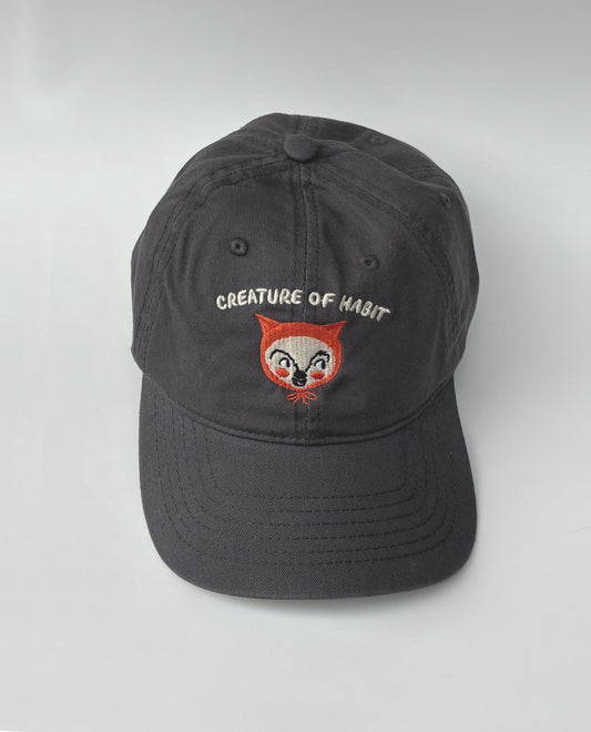 Dark gray cap with embroidered creature face and text on a white background