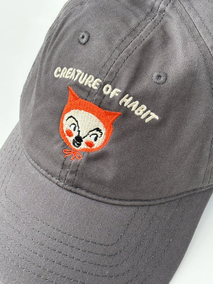 Gray cap with embroidered fox face and 'Creature of Habit' text on a white background