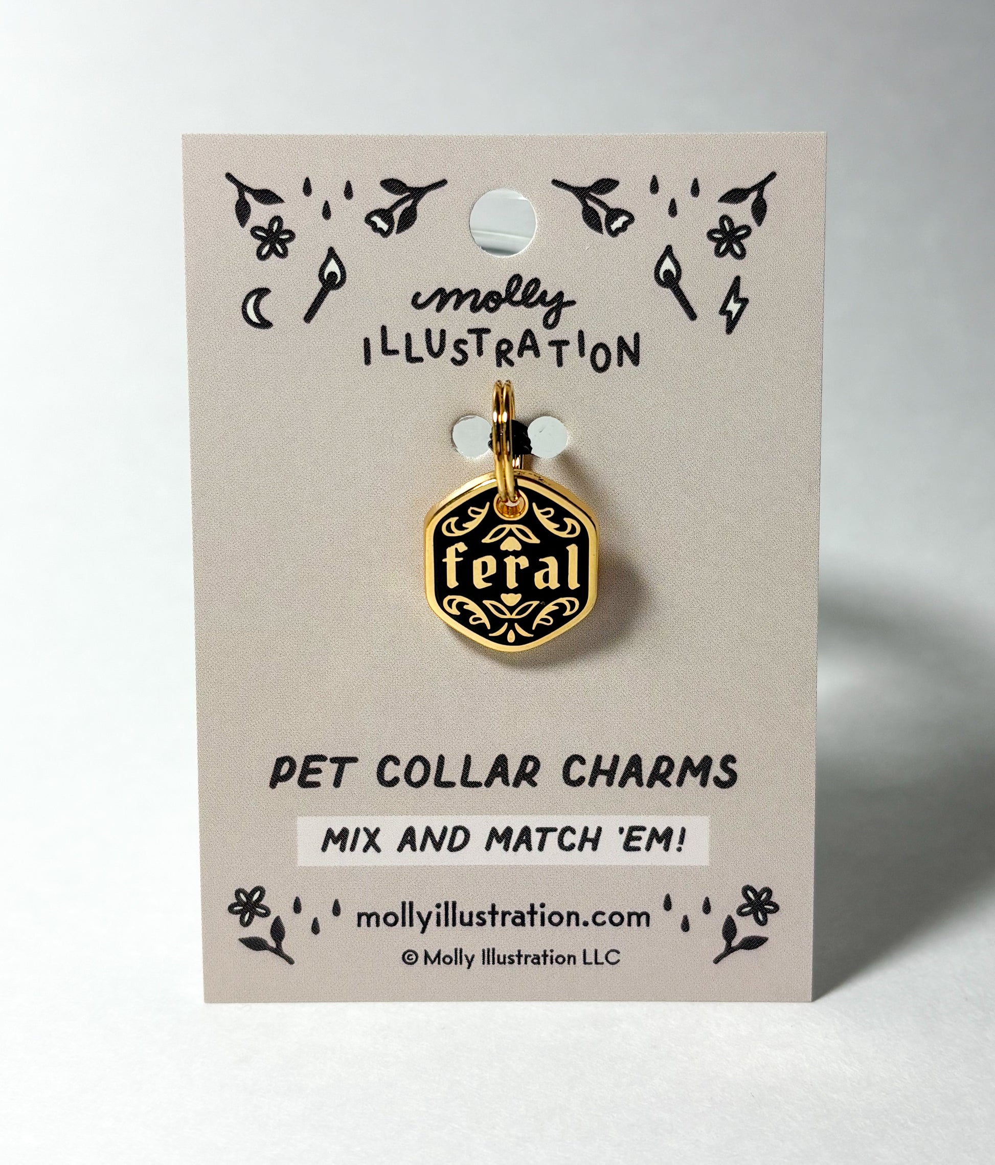 Black and gold pet collar charm that says "Feral" on a Molly Illustration backer card on a white back ground.