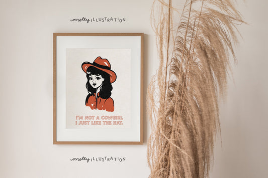 an illustrated art print of a cartoon cowgirl wearing a cowgirl hat. Beneath it is text that reads: “I’m not a cowgirl, I just like the hat.”