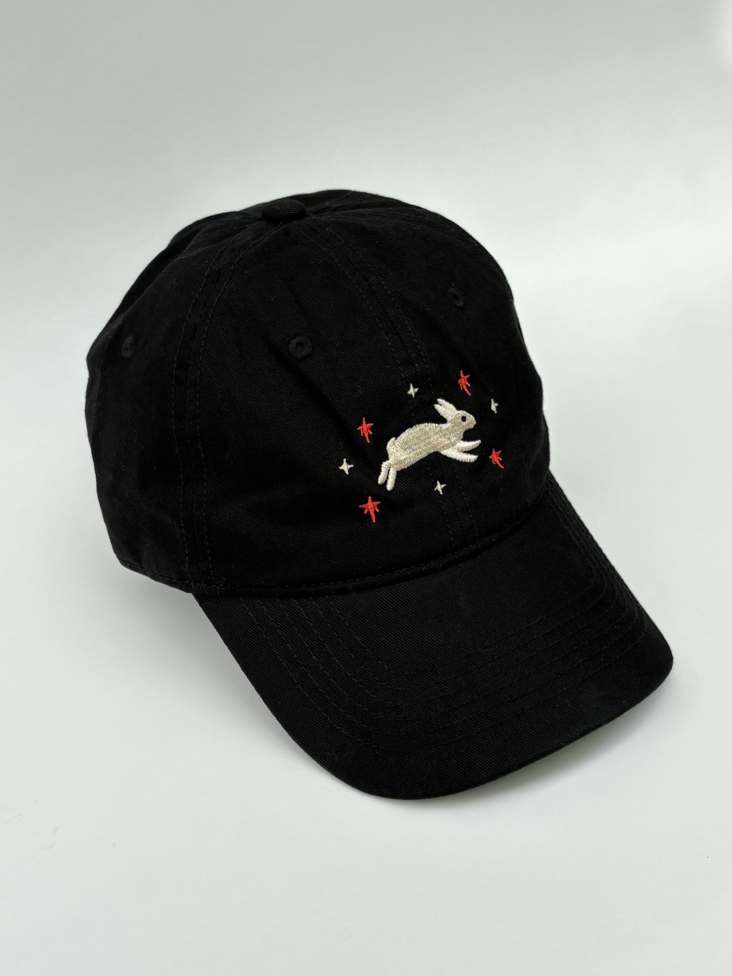 Black cap with embroidered rabbit design on a white background