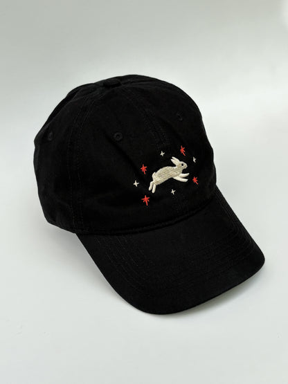 Black cap with embroidered rabbit design on a white background