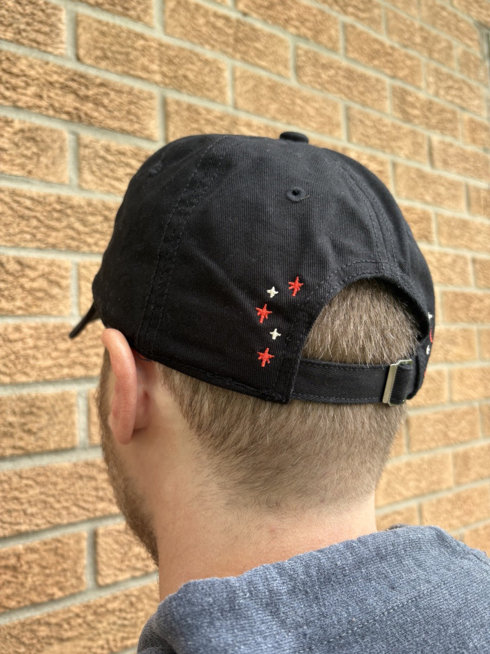 Person wearing a black cap with red and white designs against a brick wall