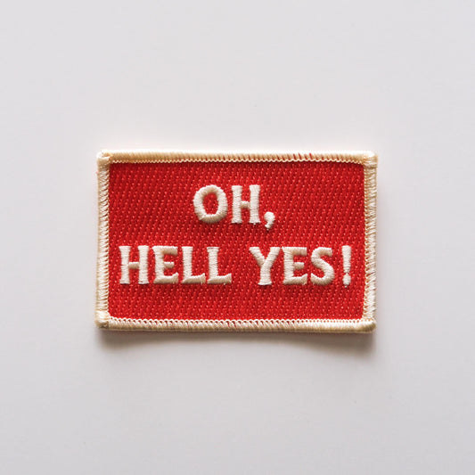 a red rectangular embroidered iron on patch that reads "Oh Hell Yes!" in off white lettering 