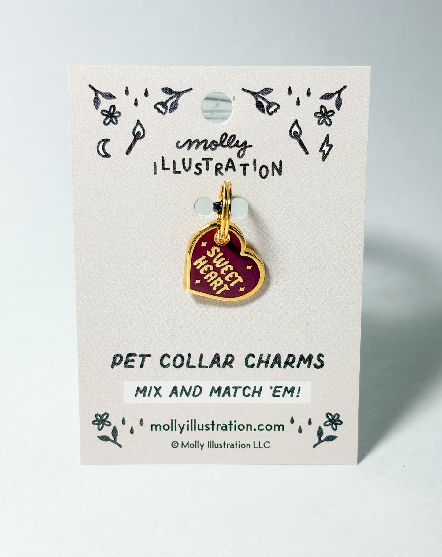 A burgundy and gold colored collar charm that reads "Sweet Heart"  on a Molly Illustration backer card 