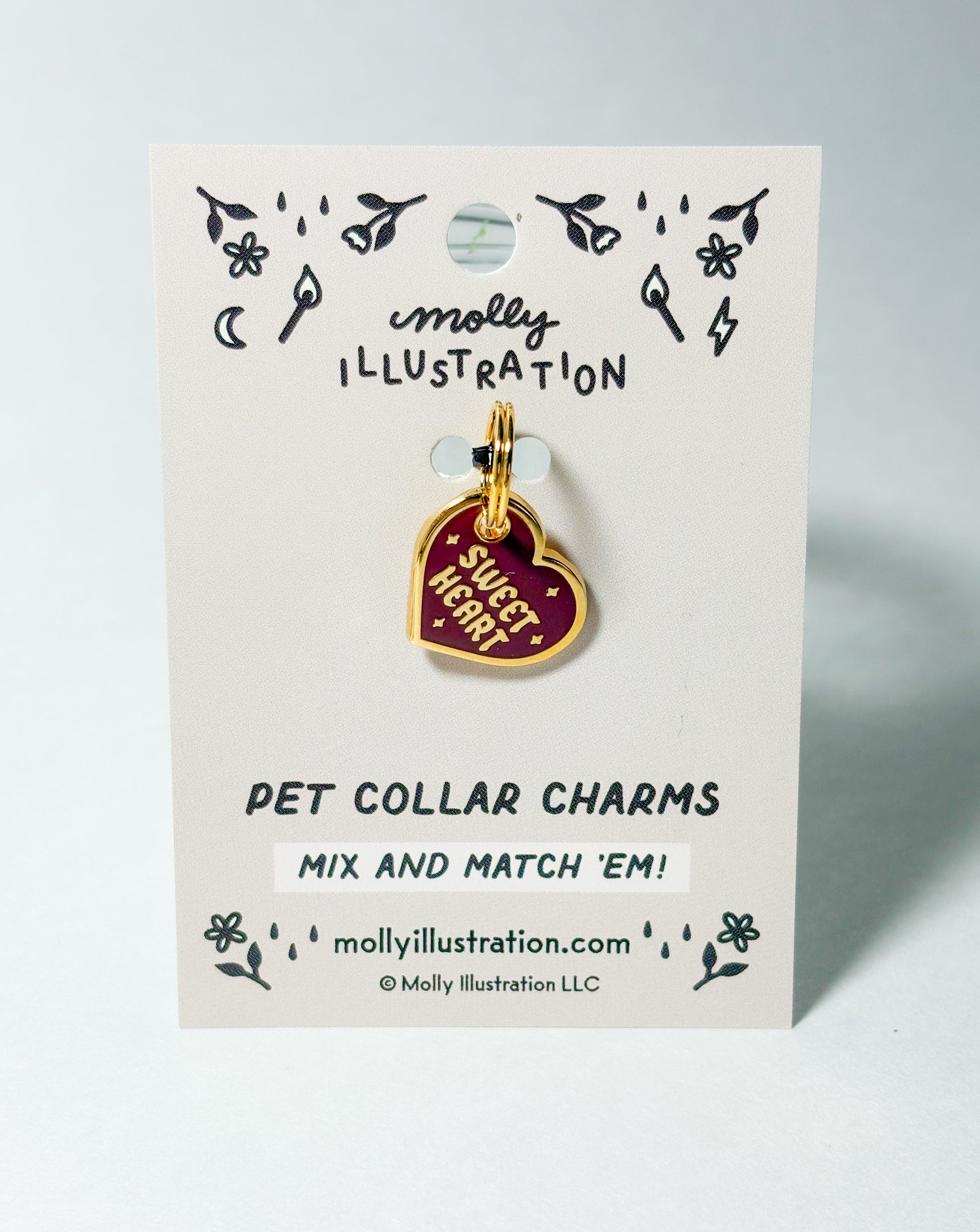 A burgundy and gold colored collar charm that reads "Sweet Heart"  on a Molly Illustration backer card 