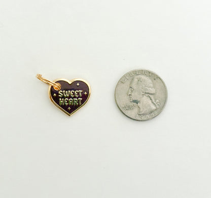 A burgundy and gold colored collar charm that reads "Sweet Heart" next to a quarter on a white background