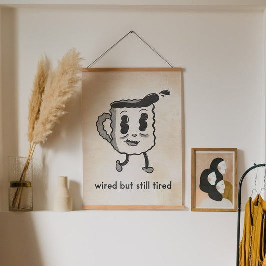 an illustrated art print of a jittery cartoon coffee cup that reads “wired but still tired” below it.