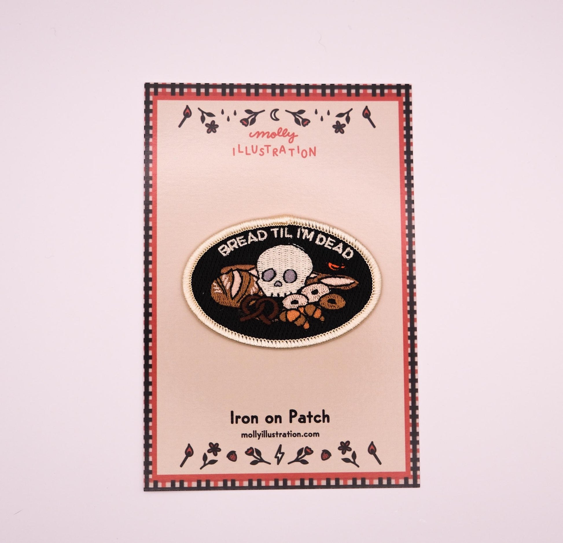 An embroidered iron on patch that reads “Bread Til I’m Dead” above various breads with a skull sitting in the middle. It is packaged on a molly illustration backer card.