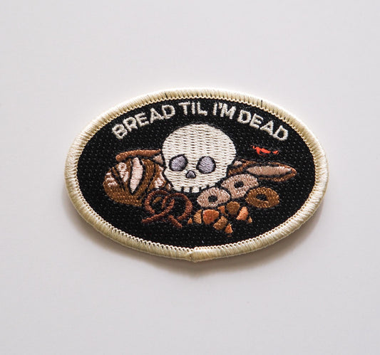 An embroidered iron on patch that reads “Bread Til I’m Dead” above various breads with a skull sitting in the middle.