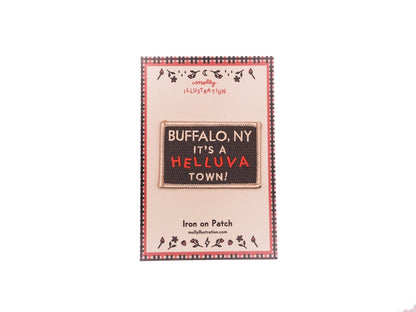 a black rectangular embroidered iron on patch that reads "Buffalo, NY It's a helluva town!" in off white and red lettering. packaged on a Molly Illustration backer card