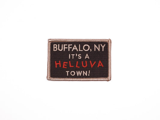 a black rectangular embroidered iron on patch that reads "Buffalo, NY It's a helluva town!" in off white and red lettering.