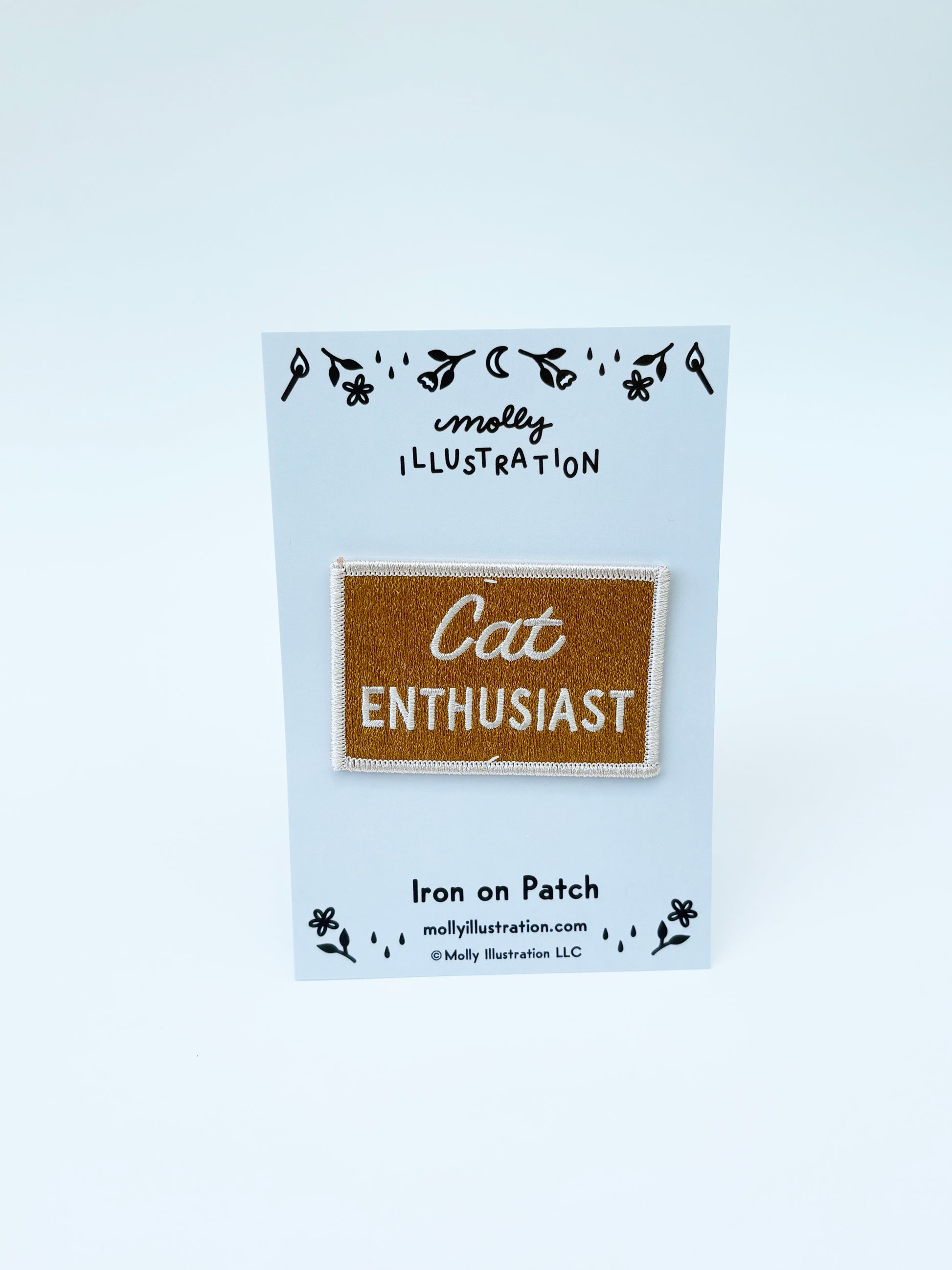 Iron on patch labeled 'Cat Enthusiast' on a blue backing card with 'molly illustration' branding.