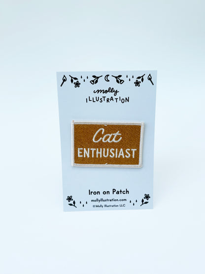 Iron on patch labeled 'Cat Enthusiast' on a blue backing card with 'molly illustration' branding.