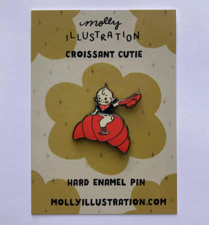 A hard enamel pin of a cartoon croissant cutie cowgirl. the background is a Molly Illustration backer card
