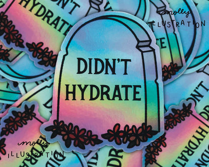 A holographic waterproof vinyl sticker of a cartoon tombstone and flowers with the phrase “Didn’t Hydrate” written on it.