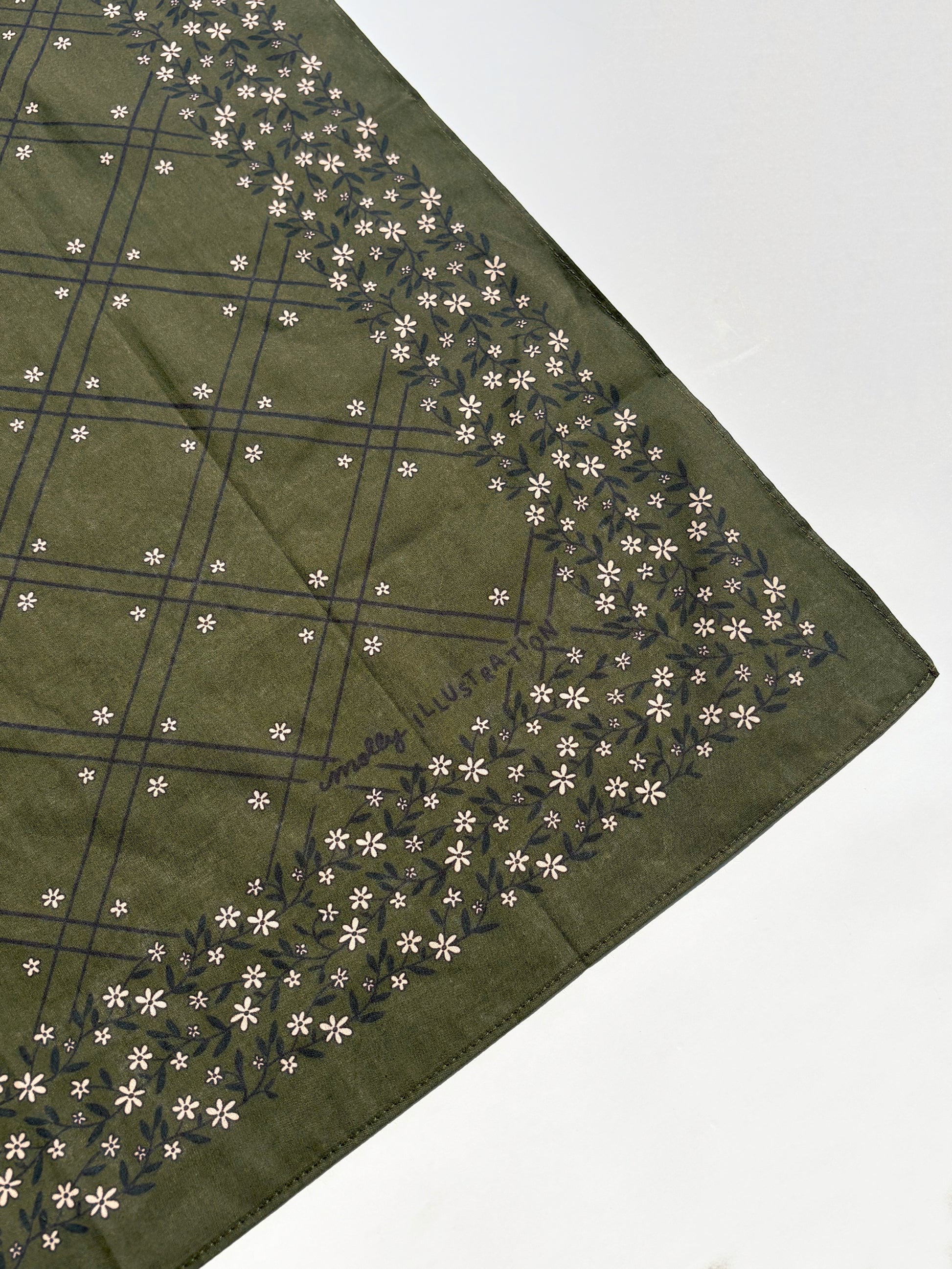 An olive green square scarf with a dark green grid pattern and a border of small white flowers, laid flat on a white surface.