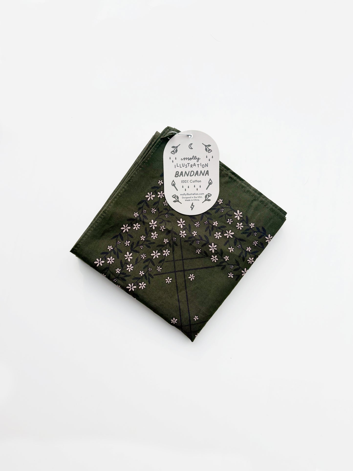 A green cotton bandana with a black grid pattern and small white floral motifs, folded with its white paper tag attached, on a clean white background.