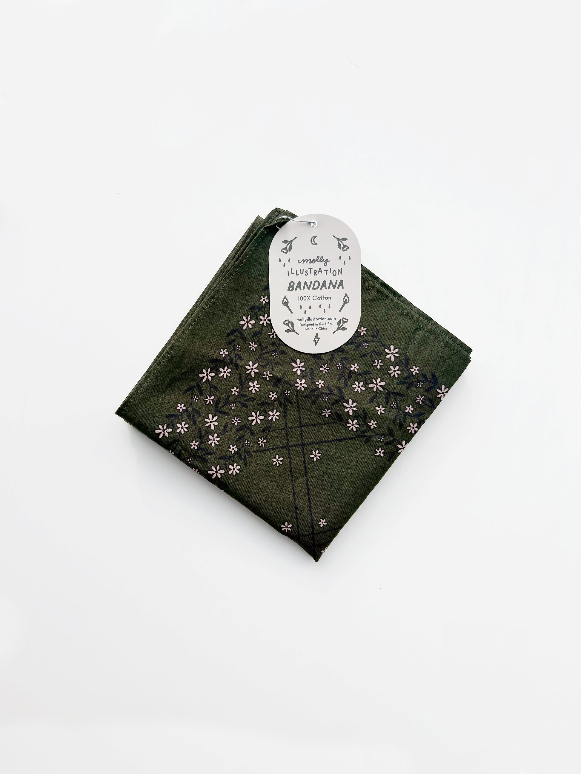 A green cotton bandana with a black grid pattern and small white floral motifs, folded with its white paper tag attached, on a clean white background.