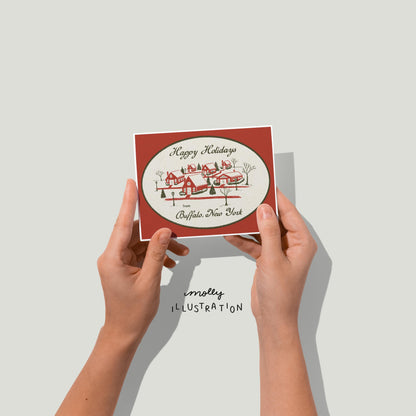 hands holding an illustrated greeting card that reads "Happy Holidays from Buffalo New York!" surrounding a red and green illustration of a snowy village.