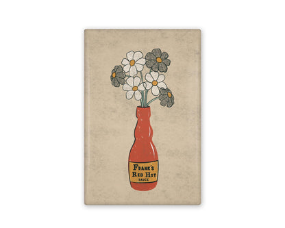 a rectangular illustrated refrigerator magnet of a frank's red hot sauce bottle that has daisies in it.