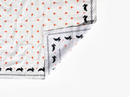 An off white bandana, featuring a pattern of small red stars, black rabbit silhouettes, and chain borders, shown with one corner folded over on a white background.