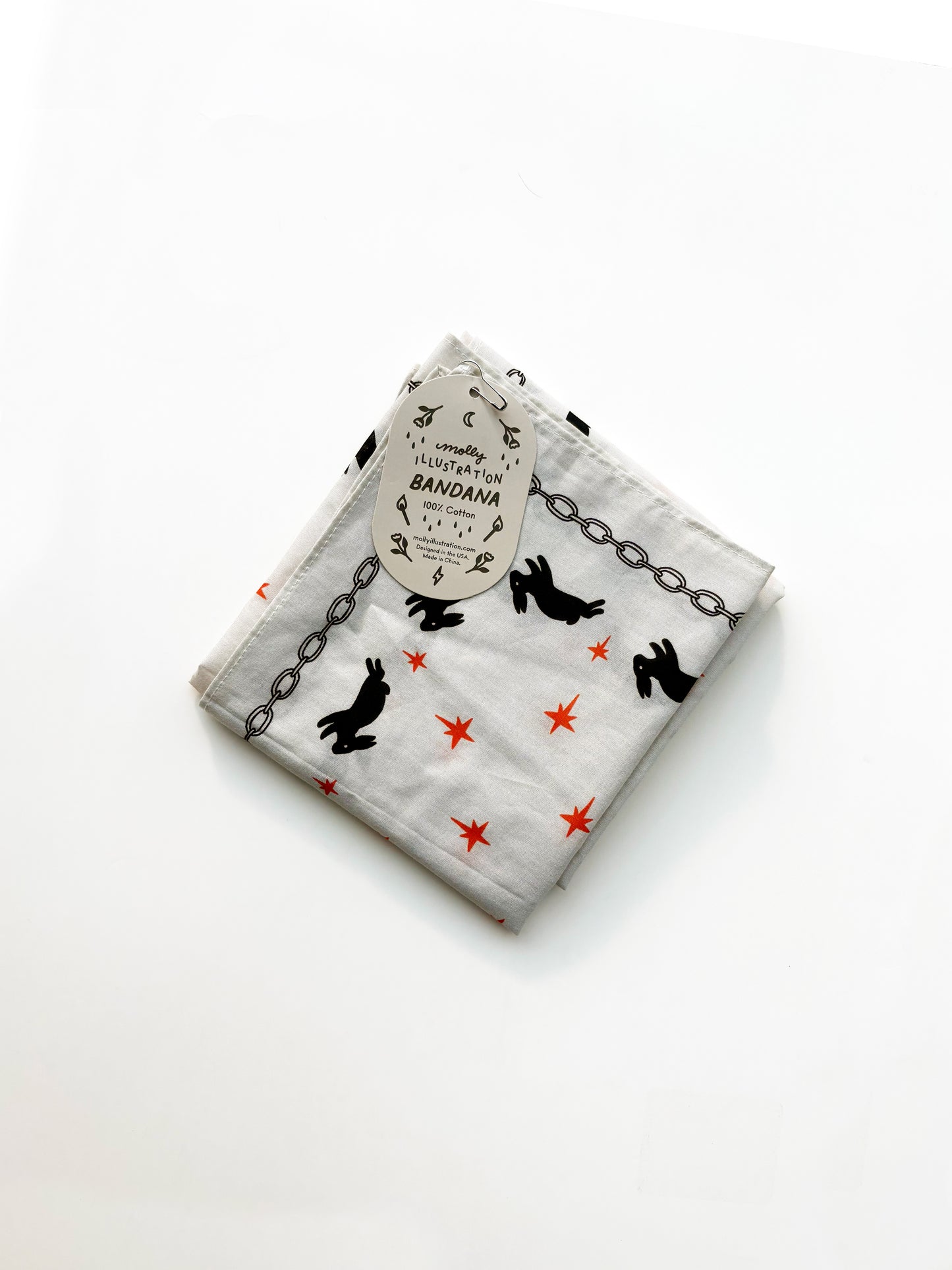 A folded white cotton bandana featuring a black rabbit and chain pattern with small red star accents, complete with a paper hangtag.