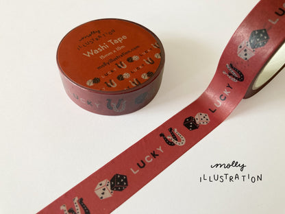 A roll of illustrated washi tape printed with the phrase “Lucky” printed on it alongside dice, and horseshoes.