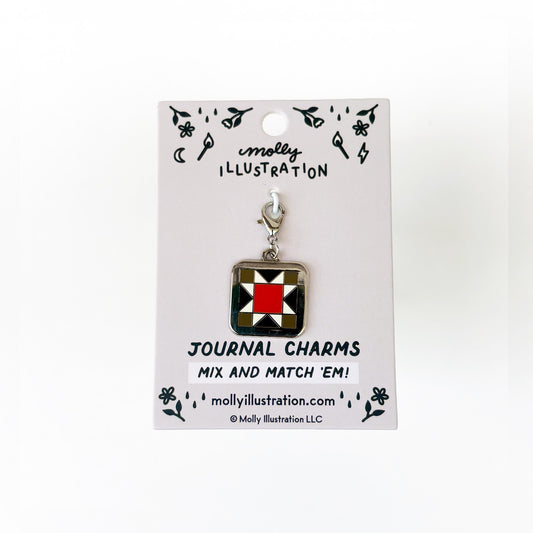 A silver, black,red and green journal charm of a quilt square. Behind it is a branded backer card for the product