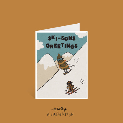 an illustrated greeting card that reads "Ski-sons Greetings" with a christmas tree and gingerbread cookie skiing down the mountain.