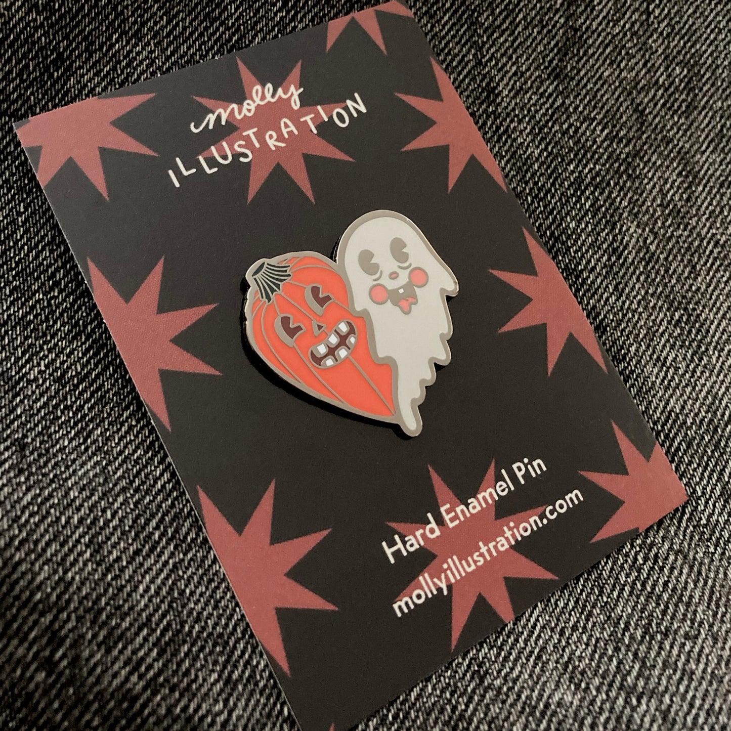 an illustrated hard enamel pin of a ghost and pumpkin on a black and orange backer card.