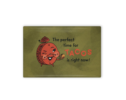 a green and red illustrated refrigerator magnet of an alarm clock holding a taco and text that reads "the perfect time for tacos is right now!" Beside it is the back view of the magnet flipped over.