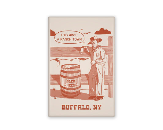 a vintage inspired illustrated magnet of a cartoon cowboy beside a barrel of bleu cheese. The text beside it reads "this ain't a ranch town." and Buffalo, NY below it.
Beside it is the back view of the magnet flipped over.