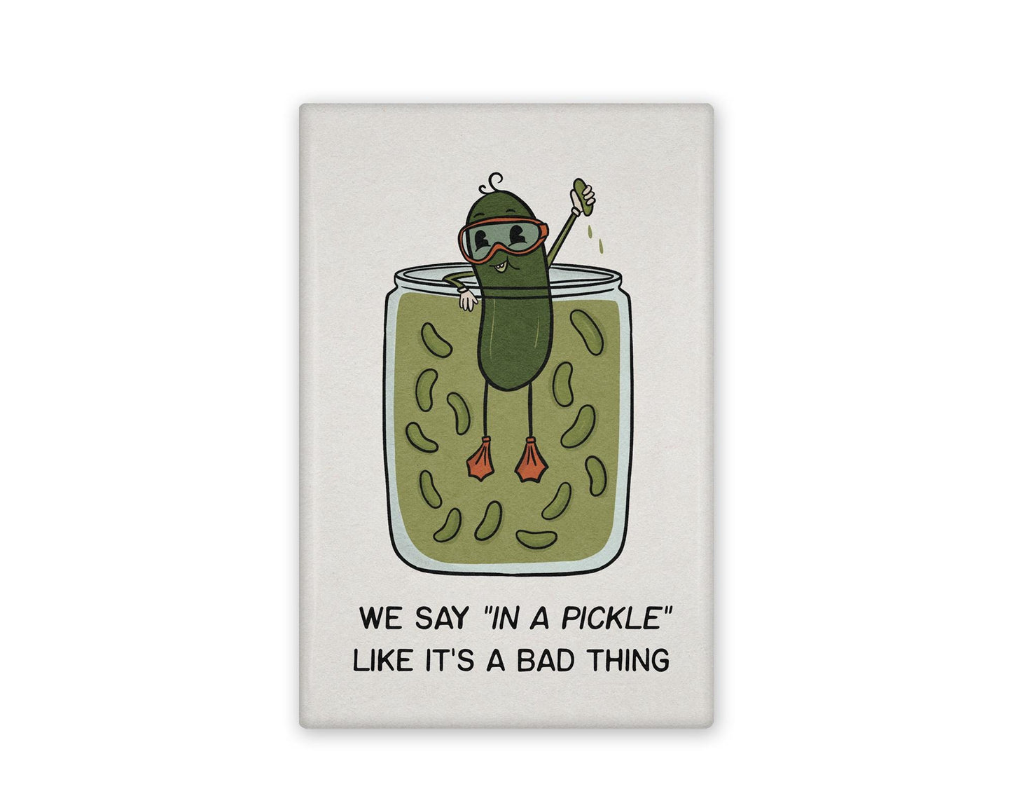 a white and green illustrated refrigerator magnet of a pickle swimming in a pickle jar that reads "We say in a pickle like it's a bad thing" Beside it is the back view of the magnet flipped over.