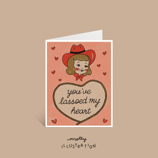 An illustrated western greeting card that reads "you've lassoed my heart" surrounded by red hearts and a cute illustrated cowgirl above the text.