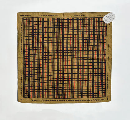 A vintage square scarf laid flat on a white background, featuring a tan border and a central black and orange checkered grid pattern. A small white paper tag is attached to the top right corner.