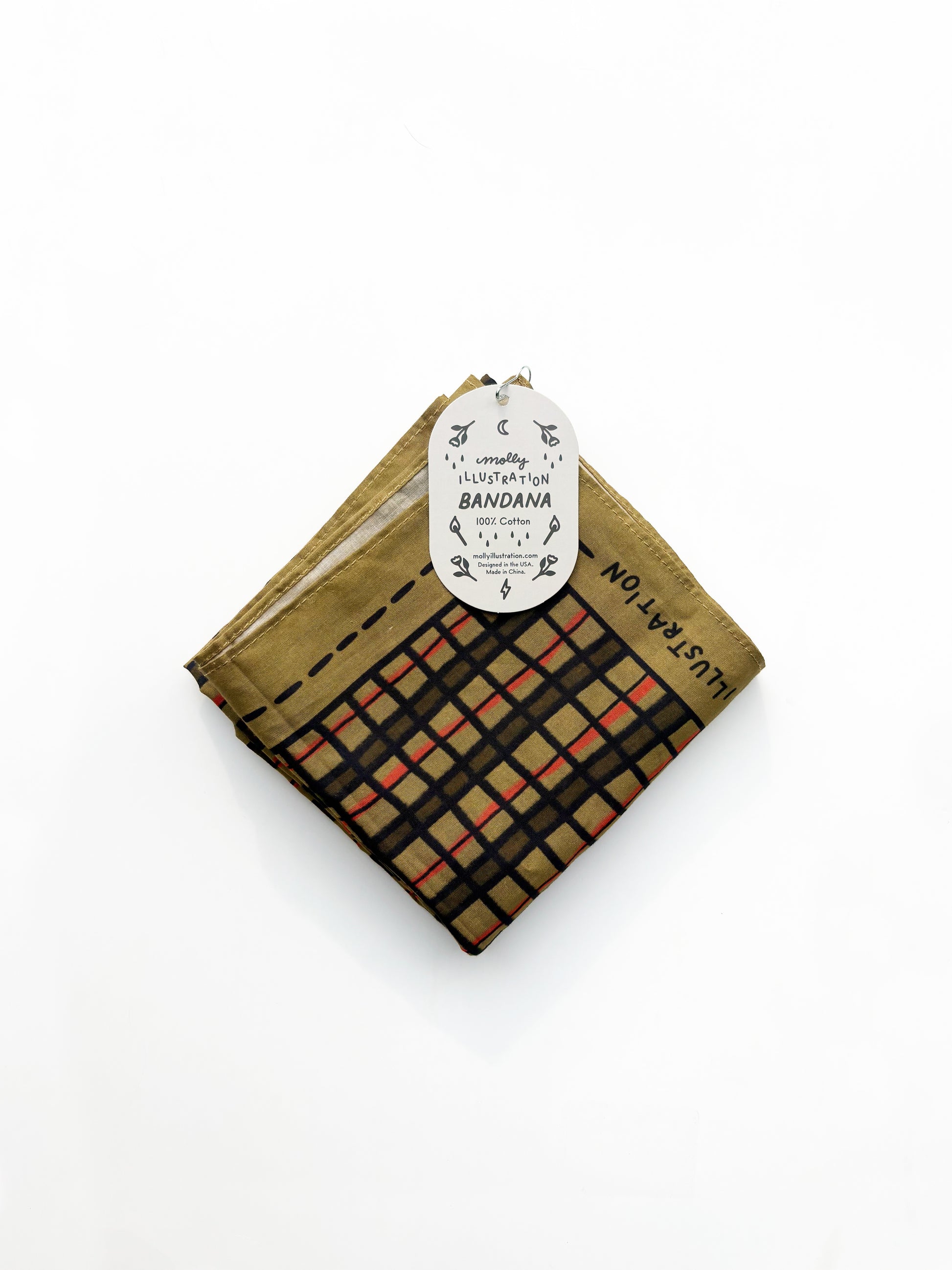 A folded cotton bandana with a plaid pattern in black, beige, and orange-red, featuring a gold-brown border and a white paper hangtag.