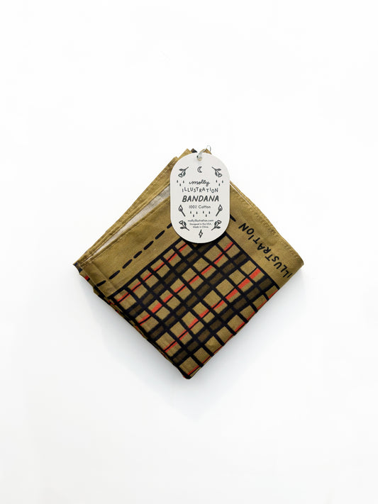 A folded cotton bandana with a plaid pattern in black, beige, and orange-red, featuring a gold-brown border and a white paper hangtag.